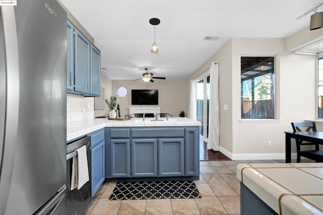 kitchen featuring blue cabinets, hanging light fixtures, tile counters, kitchen peninsula, and stainless steel appliances