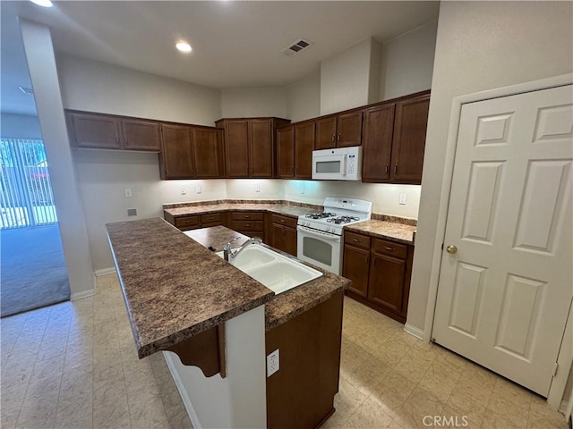 kitchen featuring a kitchen breakfast bar, sink, white appliances, a center island, and dark brown cabinetry