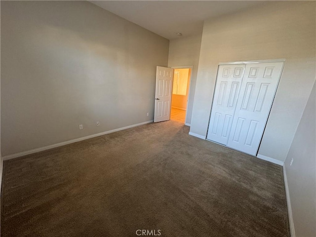 unfurnished bedroom with a closet, a towering ceiling, and dark carpet