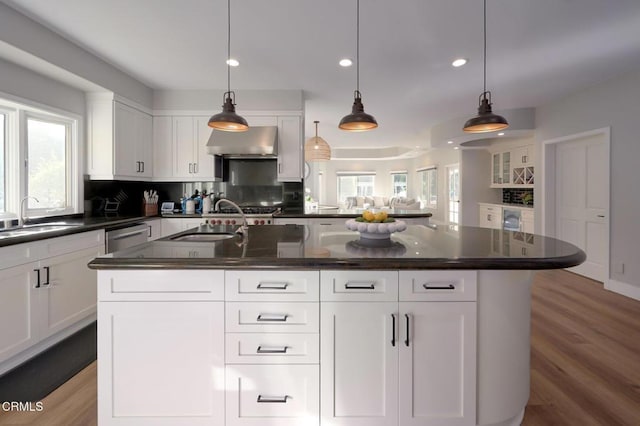 kitchen with sink, decorative light fixtures, an island with sink, and wall chimney exhaust hood