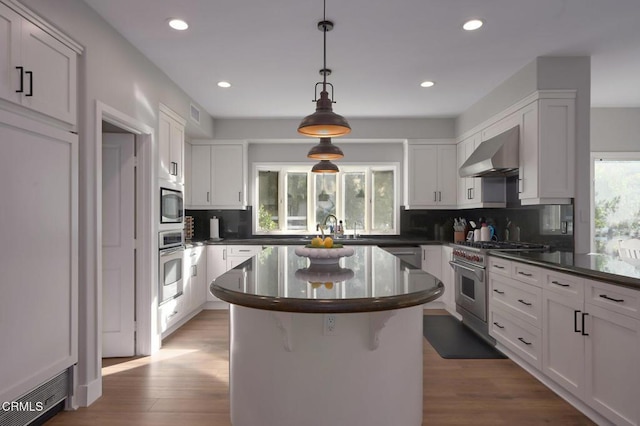 kitchen with wall chimney range hood, appliances with stainless steel finishes, white cabinetry, tasteful backsplash, and a kitchen island