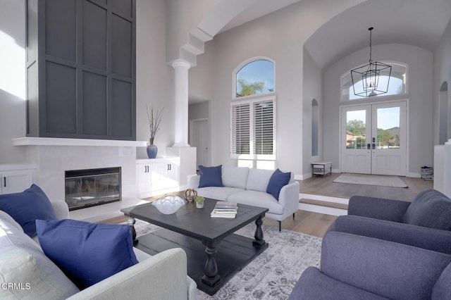 living room featuring a towering ceiling, a notable chandelier, light hardwood / wood-style floors, and french doors