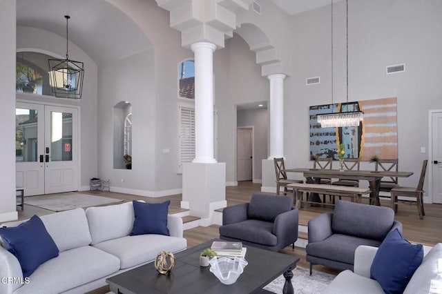 living room with decorative columns, a high ceiling, a notable chandelier, light hardwood / wood-style floors, and french doors