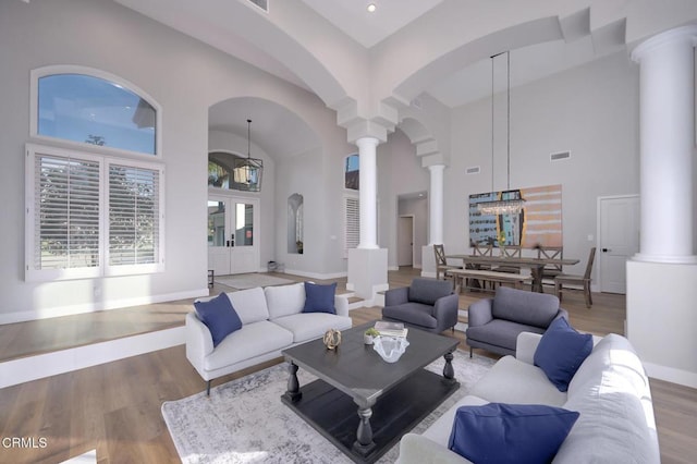 living room with french doors, a towering ceiling, decorative columns, and hardwood / wood-style floors