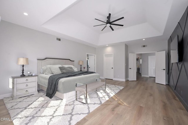 bedroom featuring light hardwood / wood-style flooring, a raised ceiling, ceiling fan, and a high ceiling