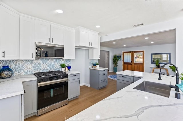 kitchen featuring sink, white cabinets, range with gas cooktop, light stone counters, and gray cabinets