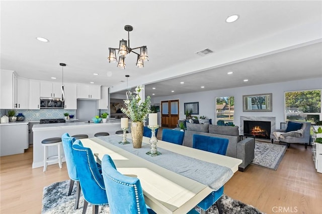 dining room with a fireplace, light hardwood / wood-style flooring, beamed ceiling, and a notable chandelier