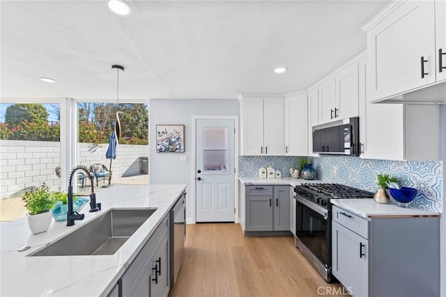 kitchen featuring pendant lighting, white cabinets, dishwasher, sink, and gas range oven