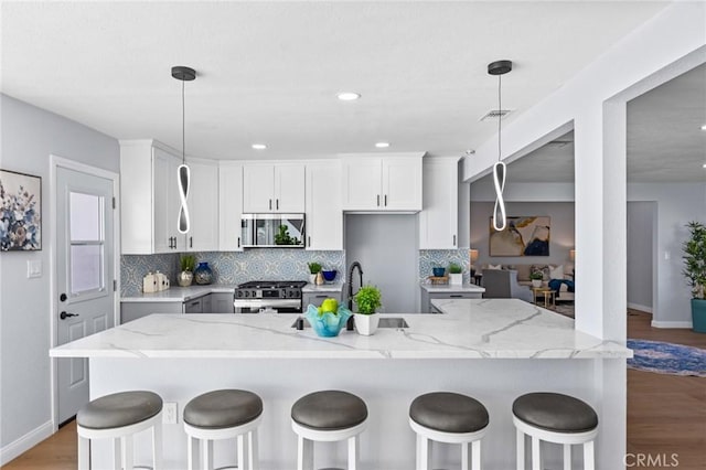 kitchen with white cabinets, pendant lighting, stainless steel gas range, and light stone counters