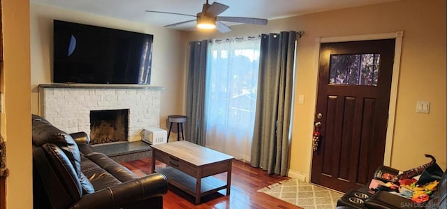 living room featuring wood-type flooring, a stone fireplace, and ceiling fan