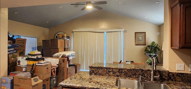 kitchen with ceiling fan, lofted ceiling, light stone countertops, and sink