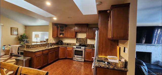 kitchen featuring a fireplace, dark stone counters, stainless steel range, kitchen peninsula, and dark wood-type flooring