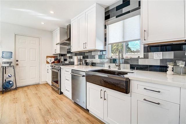 kitchen featuring light hardwood / wood-style flooring, stainless steel appliances, light stone countertops, white cabinets, and wall chimney exhaust hood