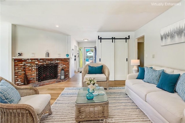 living room featuring a brick fireplace, a barn door, and light wood-type flooring