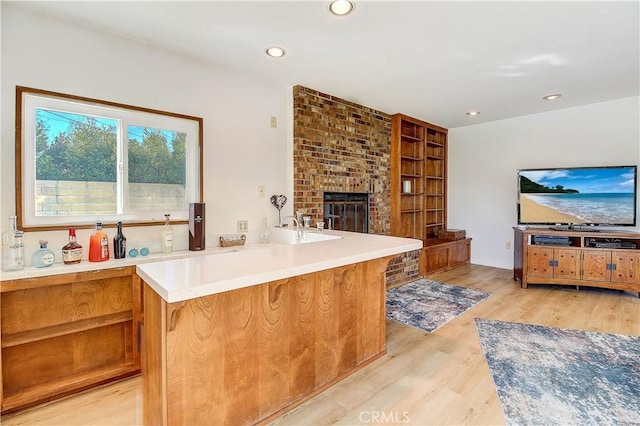 kitchen featuring a brick fireplace, light hardwood / wood-style flooring, a kitchen breakfast bar, and kitchen peninsula