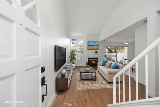 living room with baseboards, a warm lit fireplace, wood finished floors, and stairs