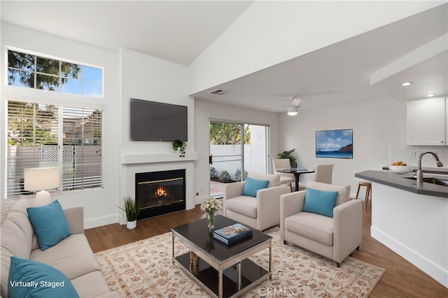 living area featuring visible vents, ceiling fan, baseboards, light wood-type flooring, and a glass covered fireplace