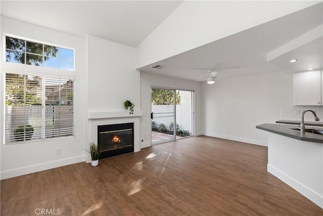 unfurnished living room featuring visible vents, baseboards, dark wood finished floors, a glass covered fireplace, and a sink