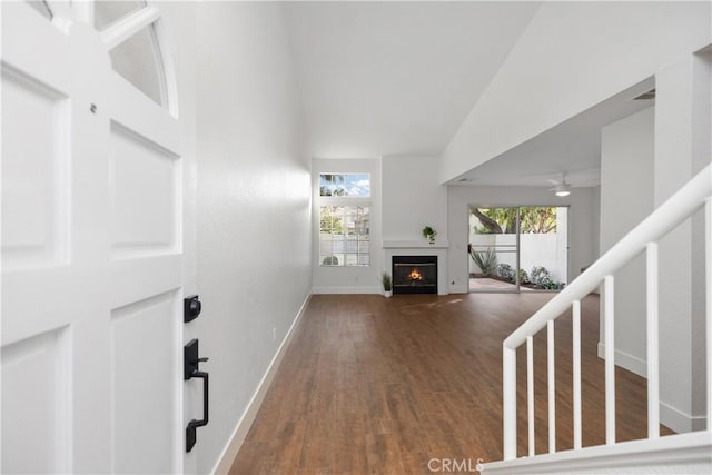 foyer with stairway, a ceiling fan, wood finished floors, baseboards, and a lit fireplace