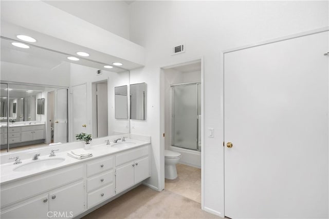 bathroom with visible vents, bath / shower combo with glass door, toilet, double vanity, and a sink