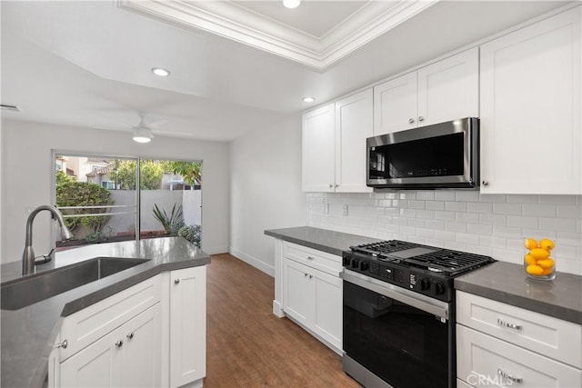 kitchen featuring a sink, stainless steel microwave, dark countertops, and gas range oven