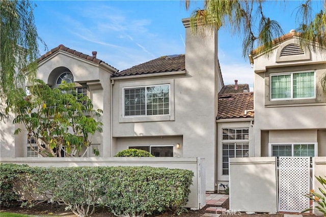 exterior space with stucco siding, a tile roof, a chimney, and fence