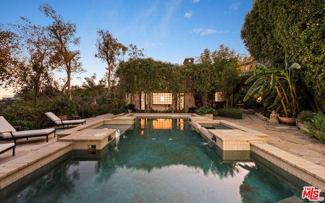 pool at dusk featuring an in ground hot tub and a patio area