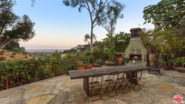 patio terrace at dusk featuring an outdoor fireplace