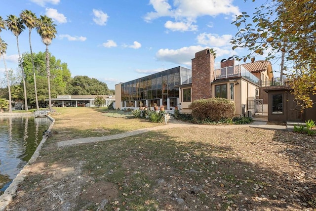 back of property featuring glass enclosure and a lawn