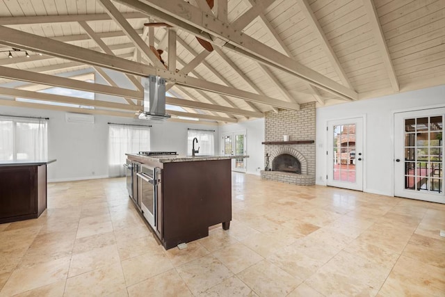 kitchen with island exhaust hood, dark brown cabinetry, a center island with sink, and beam ceiling