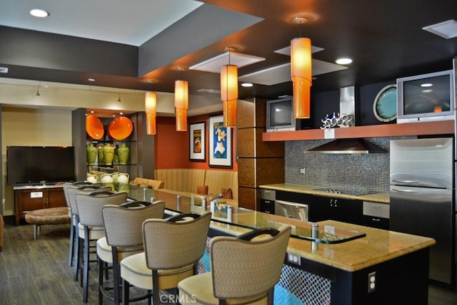 kitchen with decorative light fixtures, dark wood-type flooring, a kitchen island with sink, stainless steel refrigerator, and black electric cooktop