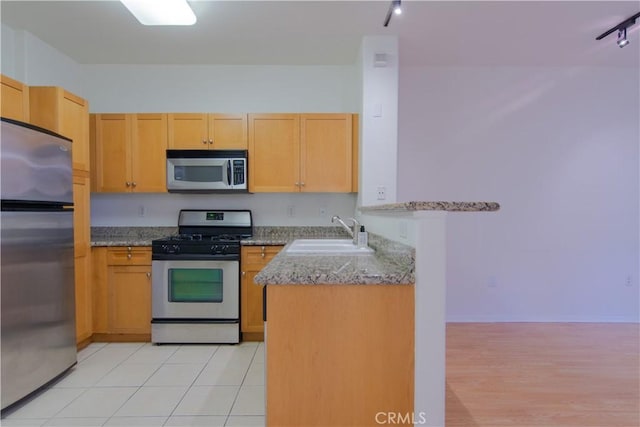 kitchen with kitchen peninsula, sink, light stone countertops, rail lighting, and stainless steel appliances