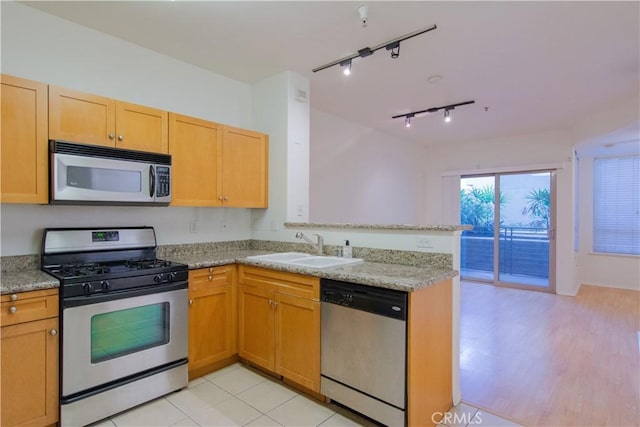 kitchen with kitchen peninsula, sink, track lighting, light stone counters, and stainless steel appliances