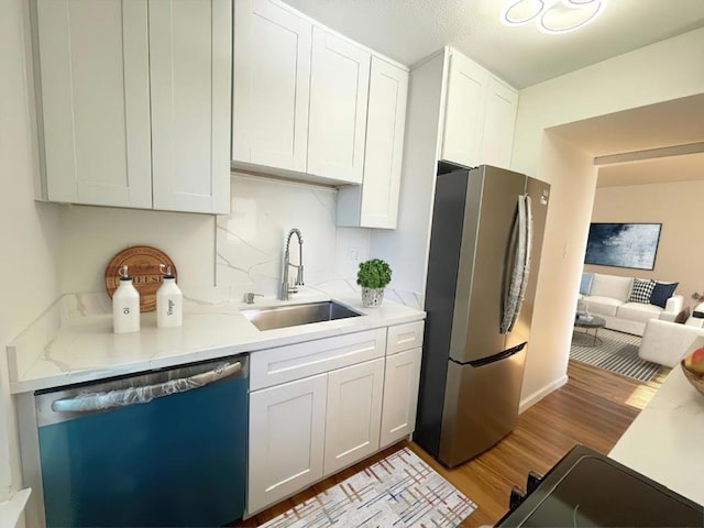 kitchen with appliances with stainless steel finishes, sink, backsplash, white cabinets, and light hardwood / wood-style floors