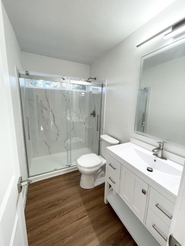 bathroom with toilet, a textured ceiling, vanity, a shower with door, and hardwood / wood-style flooring