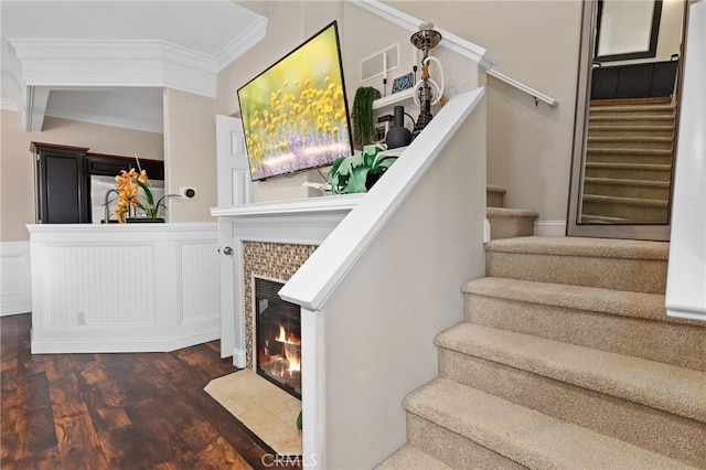 stairs with crown molding, a tiled fireplace, and hardwood / wood-style flooring