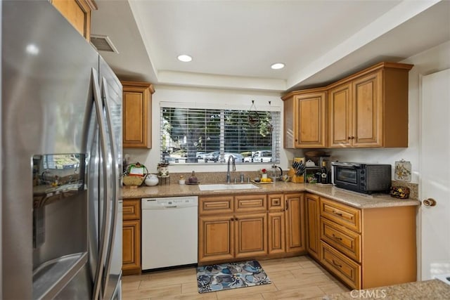 kitchen featuring sink, stainless steel fridge, dishwasher, light stone countertops, and a raised ceiling