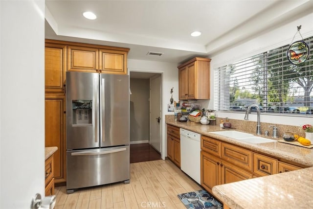 kitchen featuring dishwasher, sink, stainless steel fridge, light hardwood / wood-style floors, and light stone countertops