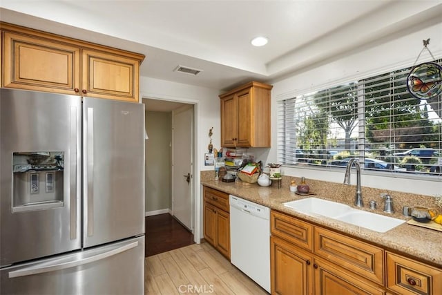 kitchen featuring dishwasher, sink, stainless steel fridge with ice dispenser, light stone countertops, and light wood-type flooring