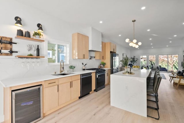 kitchen featuring light brown cabinetry, decorative light fixtures, sink, wine cooler, and black appliances