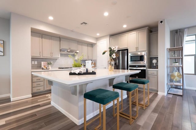 kitchen featuring a breakfast bar area, stainless steel appliances, dark hardwood / wood-style floors, an island with sink, and decorative backsplash