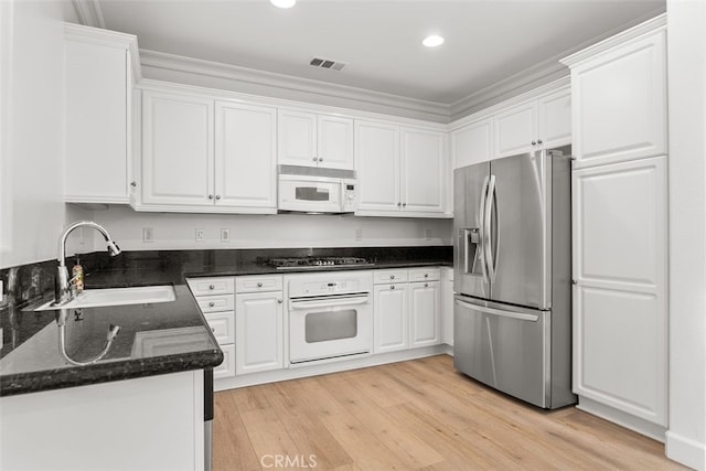 kitchen with white cabinetry, stainless steel appliances, dark stone countertops, light hardwood / wood-style floors, and sink