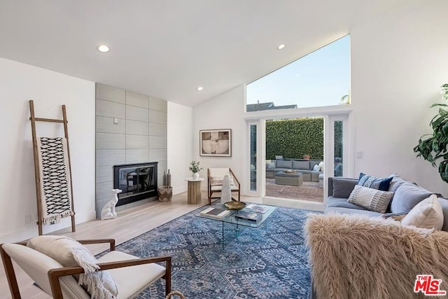 living room with a tile fireplace, high vaulted ceiling, and light hardwood / wood-style flooring