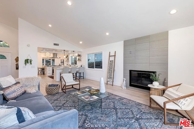 living room with a tiled fireplace, high vaulted ceiling, and light hardwood / wood-style flooring