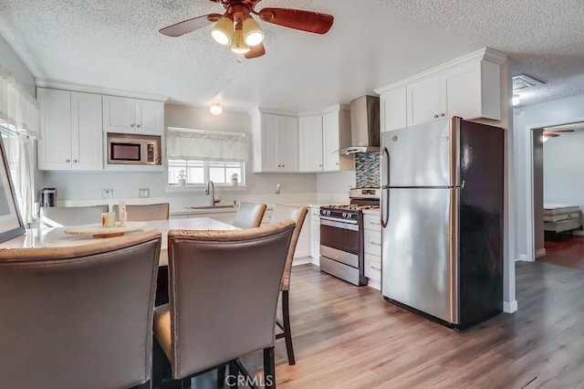 kitchen with appliances with stainless steel finishes, a kitchen breakfast bar, wall chimney range hood, white cabinets, and sink