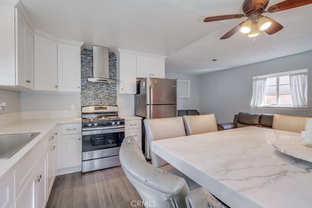 kitchen featuring light hardwood / wood-style flooring, appliances with stainless steel finishes, wall chimney exhaust hood, white cabinets, and a breakfast bar