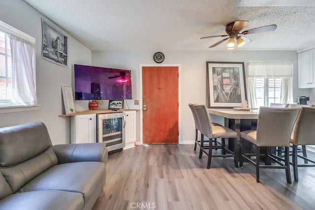 dining space featuring a textured ceiling, light hardwood / wood-style flooring, ceiling fan, bar area, and beverage cooler