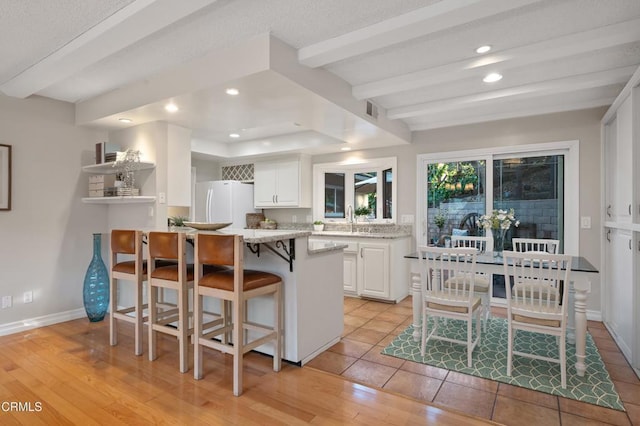 kitchen featuring white cabinets, a kitchen bar, white refrigerator, light hardwood / wood-style floors, and sink