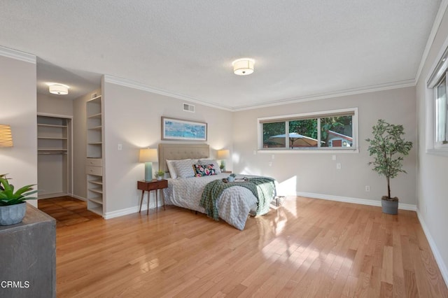 bedroom with light hardwood / wood-style floors, a textured ceiling, a spacious closet, and ornamental molding