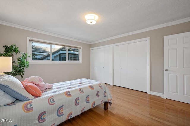 bedroom with multiple closets, light wood-type flooring, a textured ceiling, and ornamental molding